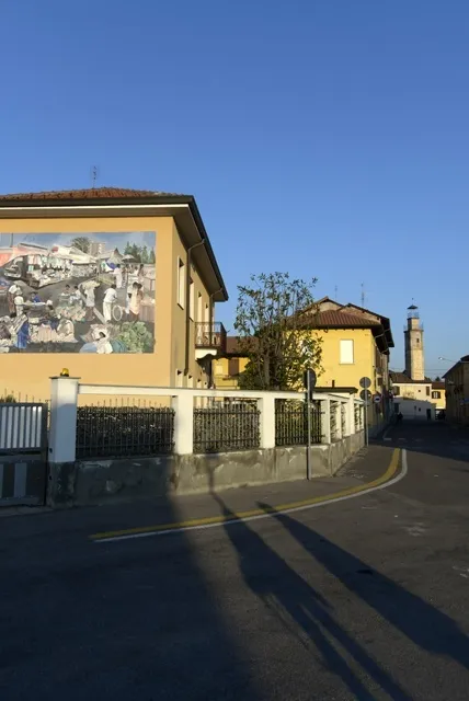 Scorcio di Dairago, si intravvede il murale 'Mercato globale' (1995) e le ombre dei giornalisti Salvatore Giannella e Benedetta Rutigliano.