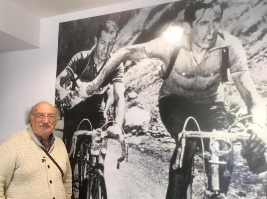 Salvatore Giannella accanto alla gigantografia della foto di Carlo Martini che testimonia il passaggio della borraccia tra Coppi e Bartali sul passo del Galibier nel Tour de France, ore 15 del 6 luglio 1952