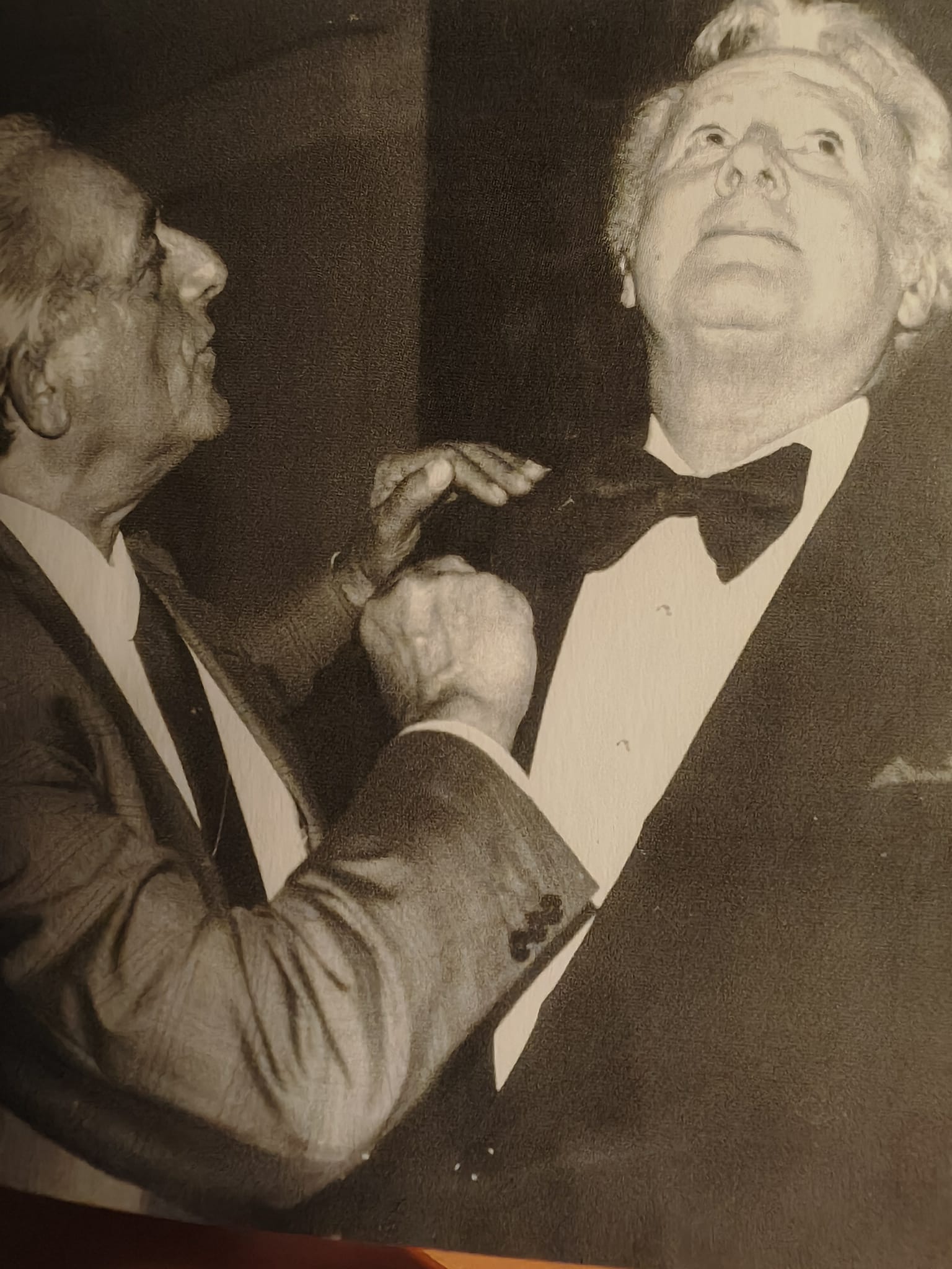 Foto in bianco e nero: Francesco Leoni, di profilo a sinistra, sistema il papillon all'attore Van Johnson in smoking.